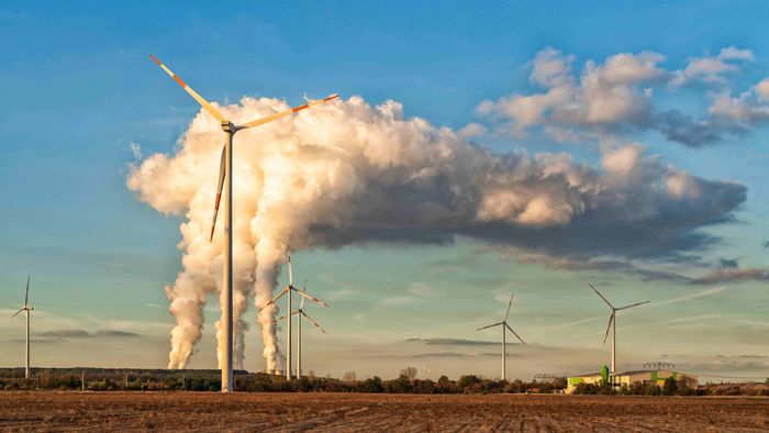 Zu sehen sind Windräder auf einem Feld mit einem Braunkohleabbau im Hintergrund.