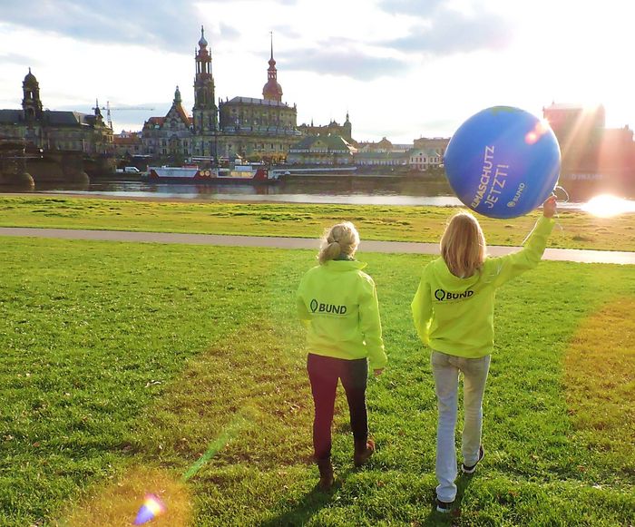 Zwei Frauen mit grüner BUND Jacke und blauem Luftballon laufen Richtung Elbe