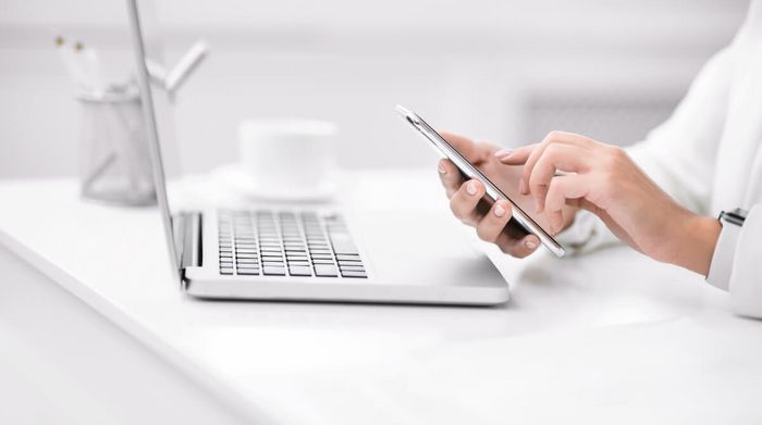 Person sitzt vor einem Laptop mit einem Handy in der Hand.